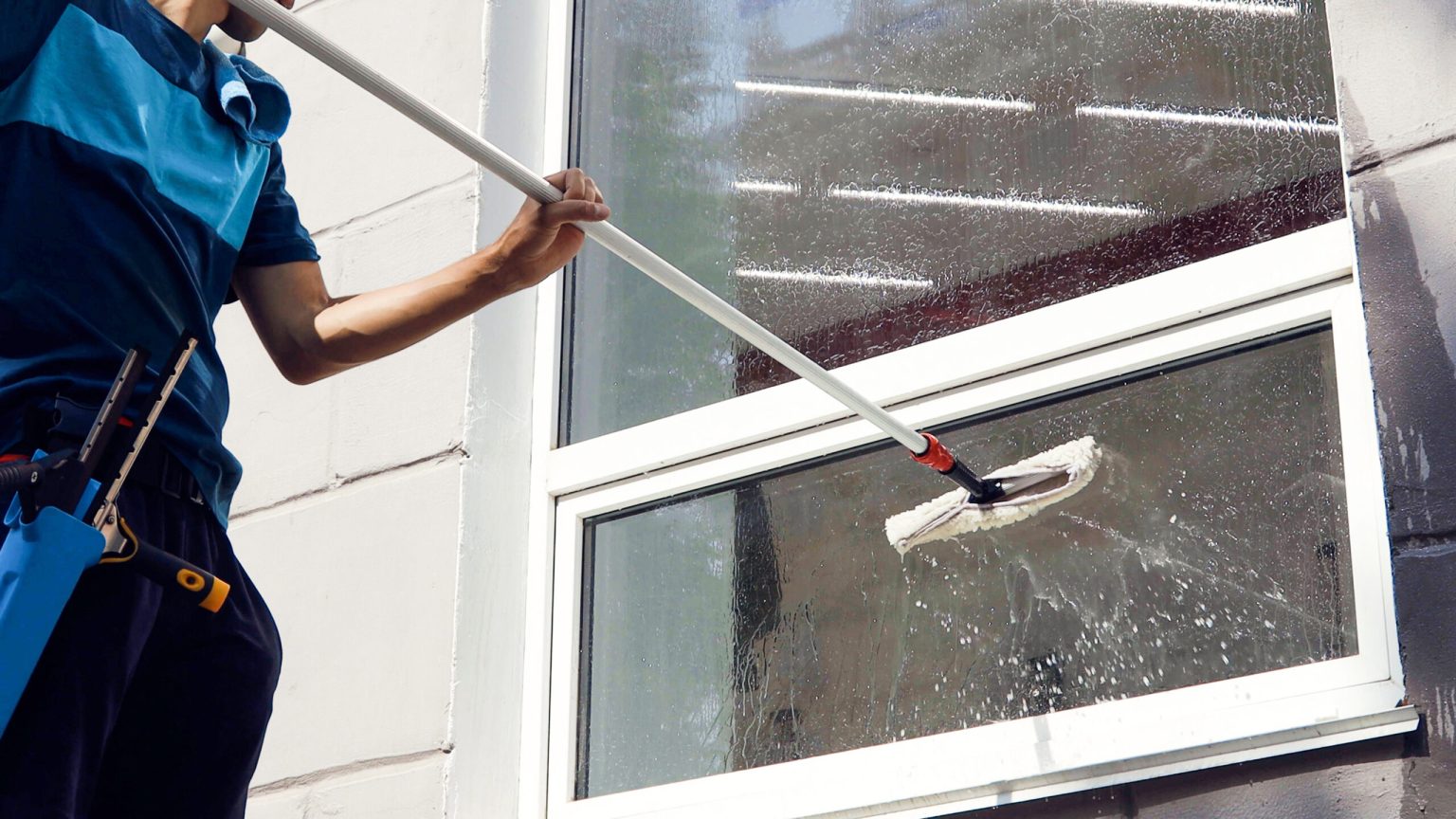 Male professional cleaning service worker in overalls cleans the windows and shop windows of a store with special equipment.